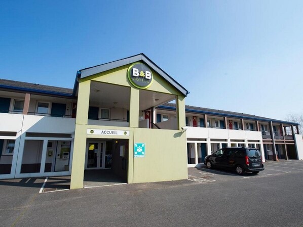 Un gîte ou une chambre d’hôtes avec une enseigne indiquant « ACCUEIL », un parking et un bâtiment en arrière-plan.