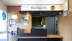 A reception desk with a 'Bienvenue chez B&B' sign, a security kiosk, and a fire extinguisher. - B&B Hotel Tours Nord 1 Val De Loire (Tours)