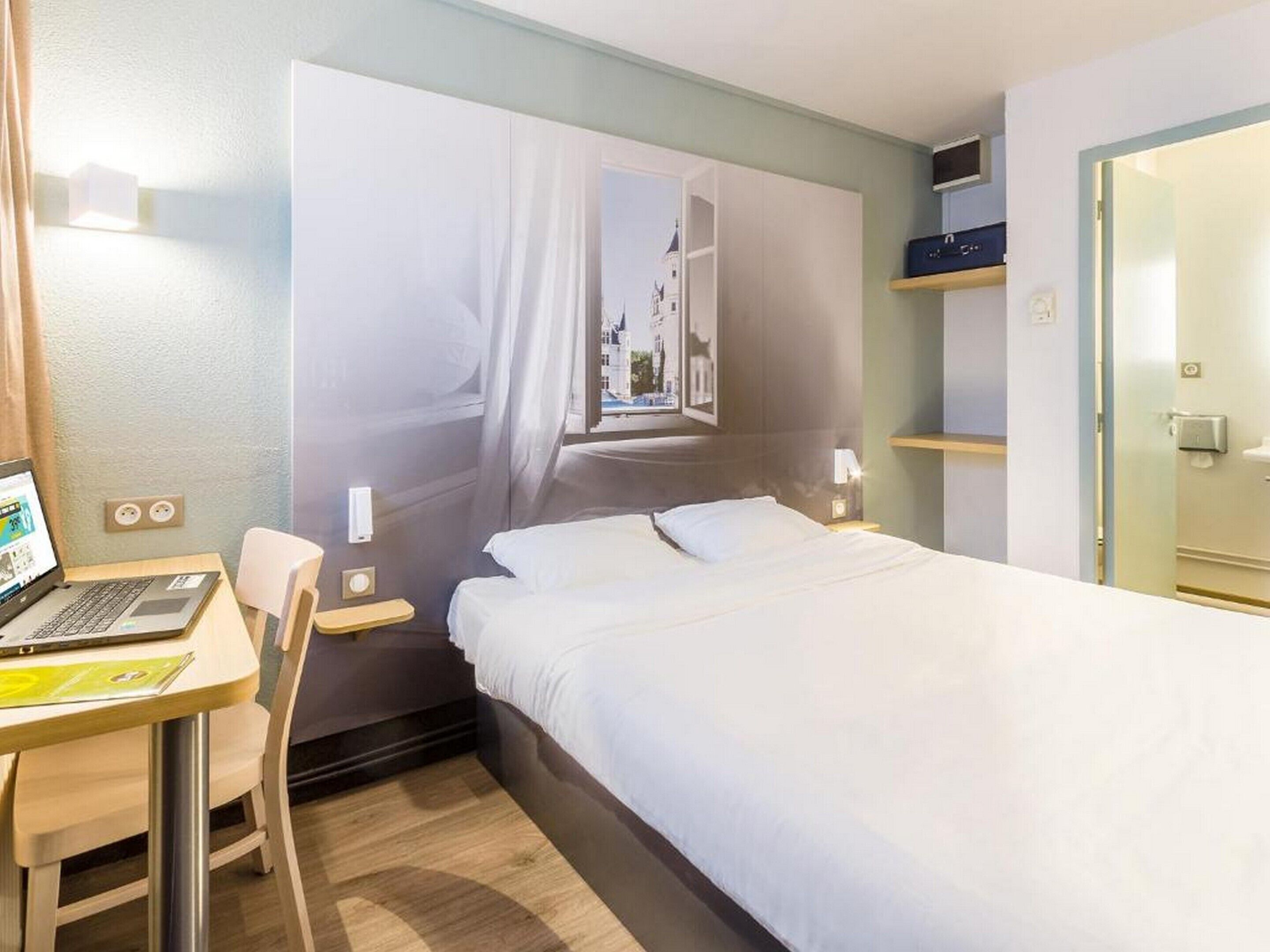 Habitación de hotel con cama, escritorio con una computadora portátil, silla, ventana con vista y puerta.