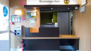 A reception desk with a 'Bienvenue chez B&B' sign, a security kiosk, and a fire extinguisher.