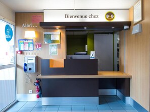 A reception desk with a 'Bienvenue chez B&B' sign, a security kiosk, and a fire extinguisher. - B&B Hotel Tours Nord 1 Val De Loire (Tours)