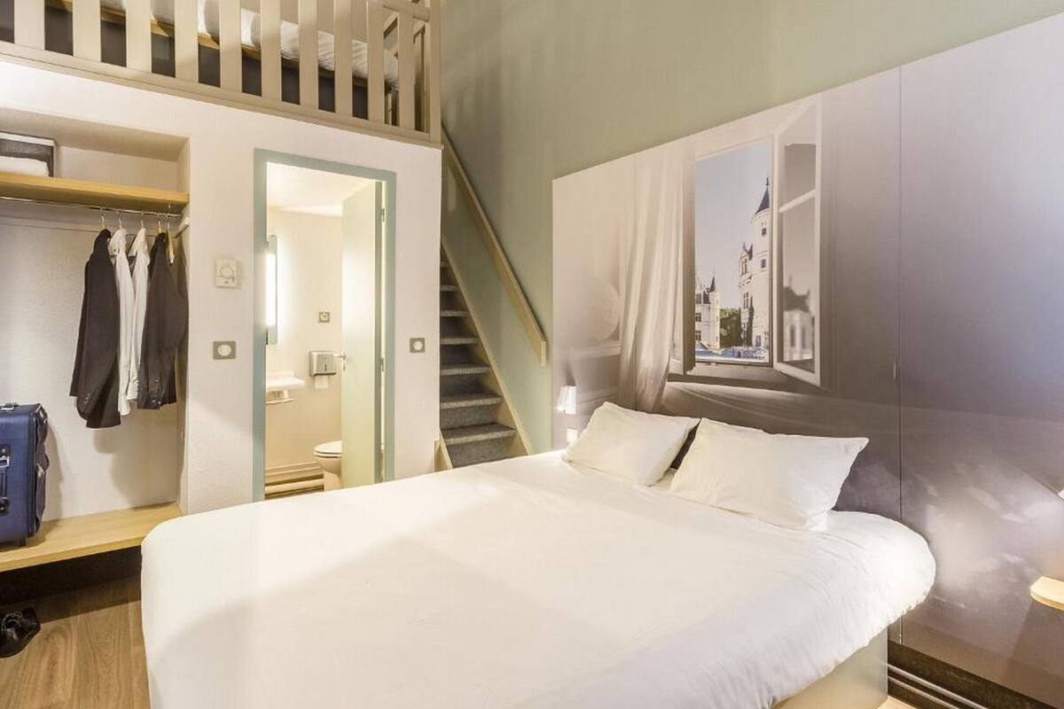 A hotel room with a bed, a wardrobe, a mirror, a bathroom, and a staircase.
