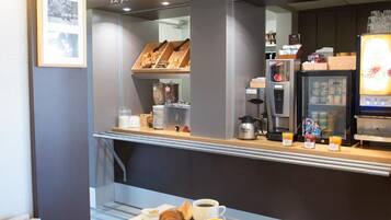 Een ontbijtbuffet met croissants, sap en koffie, en een bordje erboven met de tekst 'Le petit-déjeuner, comme chez vous'.