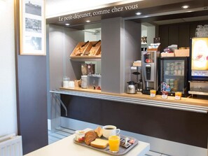 A breakfast counter with croissants, juice, and coffee, and a sign above reading 'Le petit-déjeuner, comme chez vous'. - B&B Hotel Tours Nord 1 Val De Loire (Tours)