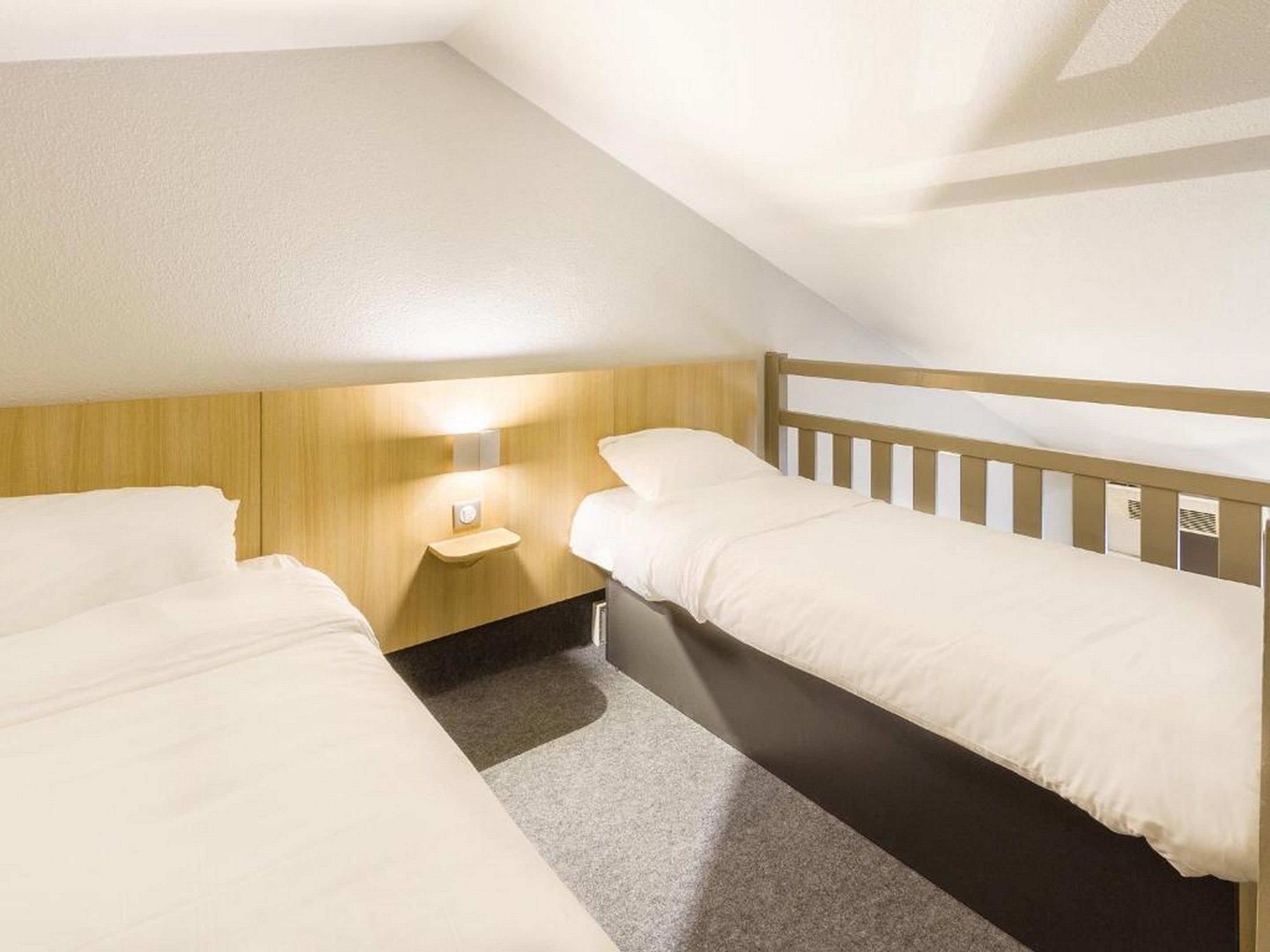 A small, single-room hotel with two beds, a nightstand, and a wall-mounted light.