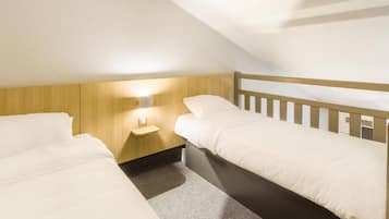 A small, single-room hotel with two beds, a nightstand, and a wall-mounted light.