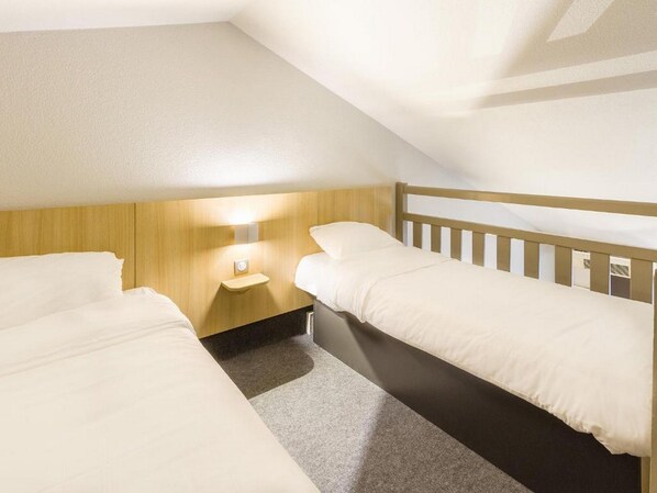 A small, single-room hotel with two beds, a nightstand, and a wall-mounted light. - B&B Hotel Tours Nord 1 Val De Loire (Tours)