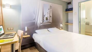 Quarto de hotel com cama, uma escrivaninha com um laptop, uma cadeira, uma janela com vista e uma porta.