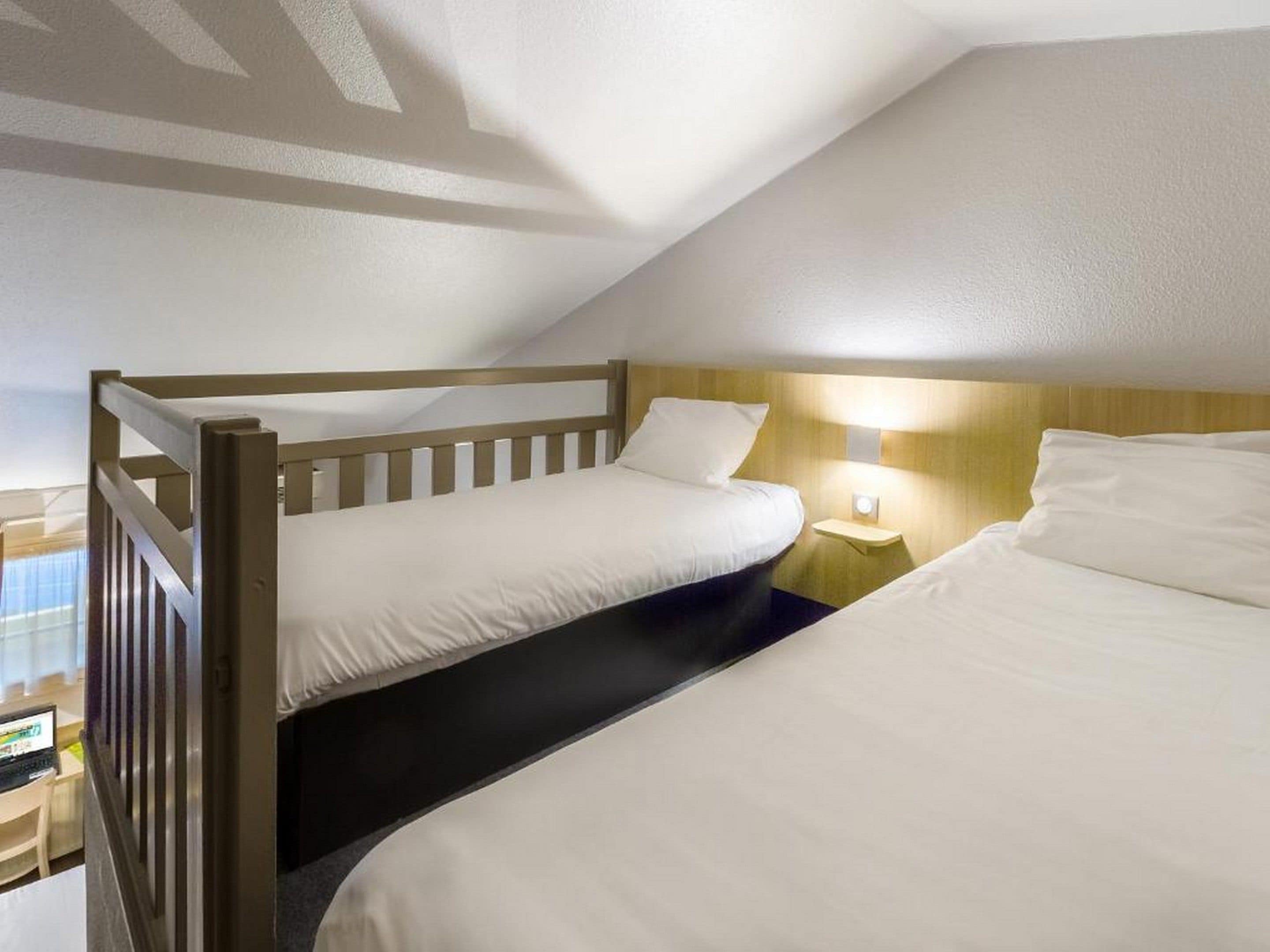 Une chambre avec deux lits, une tête de lit en bois, une table de chevet avec une lampe et une fenêtre avec des stores.
