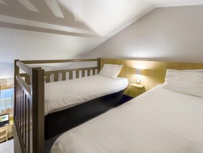 Una habitación con dos camas, cabecero de madera, mesita de noche con lámpara y ventana con persianas.