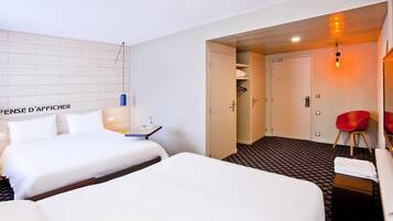 Habitación de hotel con dos camas, un escritorio, una silla, un armario y un pequeño rincón de descanso con una silla roja.