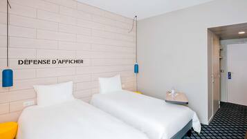 A hotel room with two beds, a wall-mounted light fixture, and a door leading to another room.
