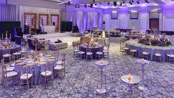 Une salle de banquet avec des tables rondes, des chaises et une scène équipée de matériel de sonorisation.