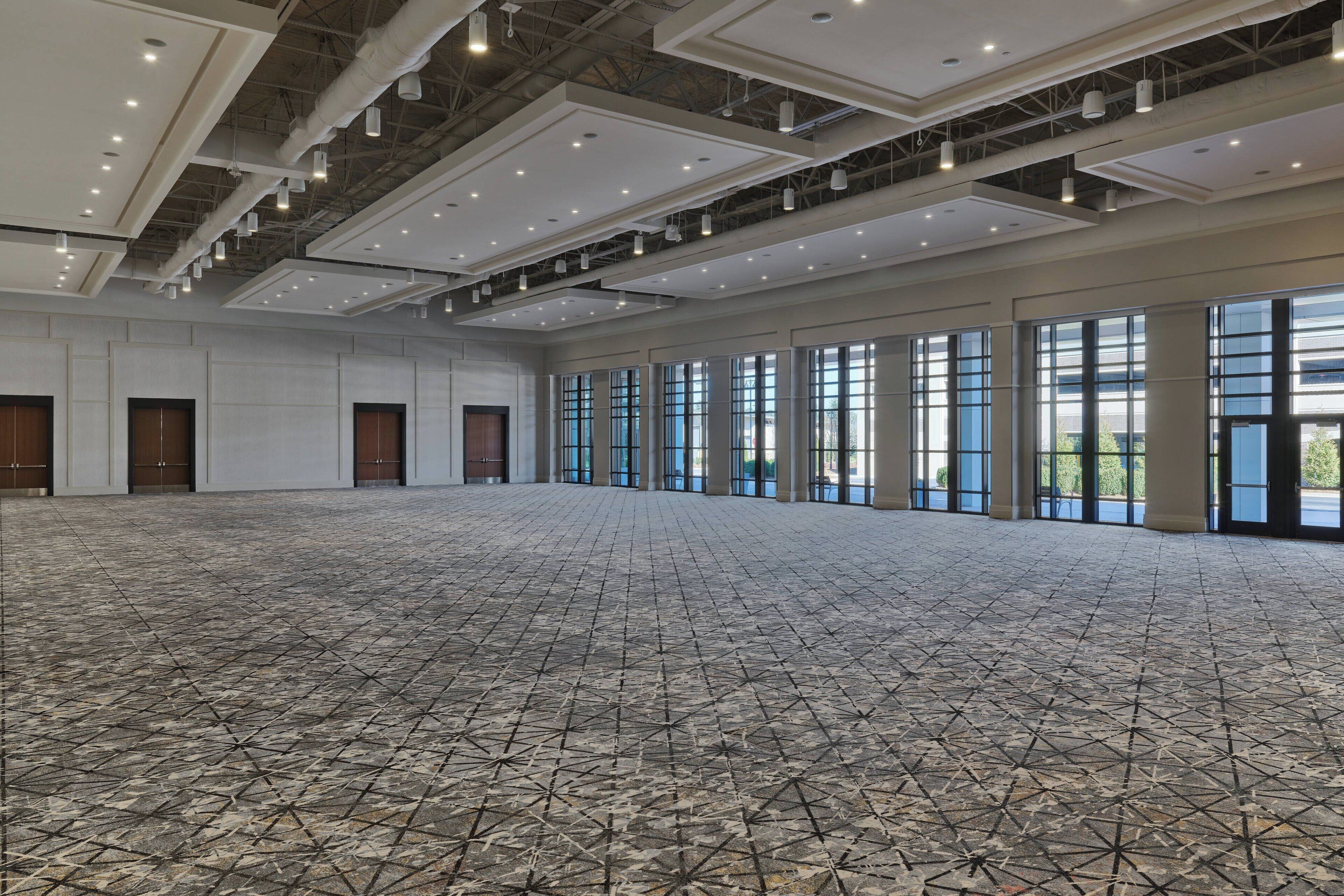 A spacious hall with a geometric patterned floor, large windows, and a high ceiling with exposed beams and lighting fixtures.