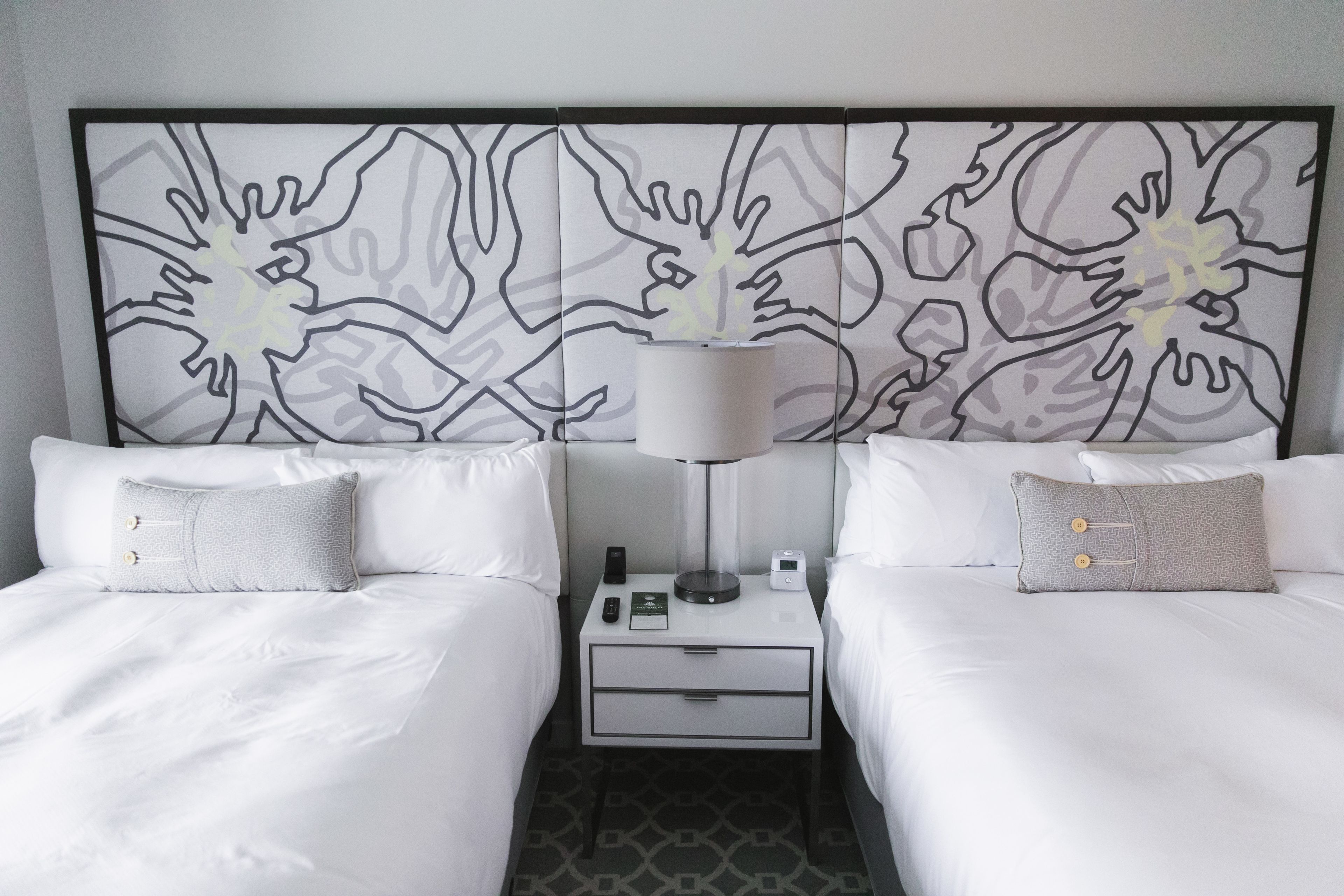 A hotel room with two beds, a nightstand with a lamp, a phone, and a small table.