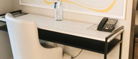 A modern office space with a white desk, a white chair, a large abstract painting on the wall, a bottle of water, and a telephone.