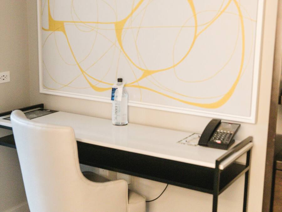 A modern office space with a white desk, a white chair, a large abstract painting on the wall, a bottle of water, and a telephone.