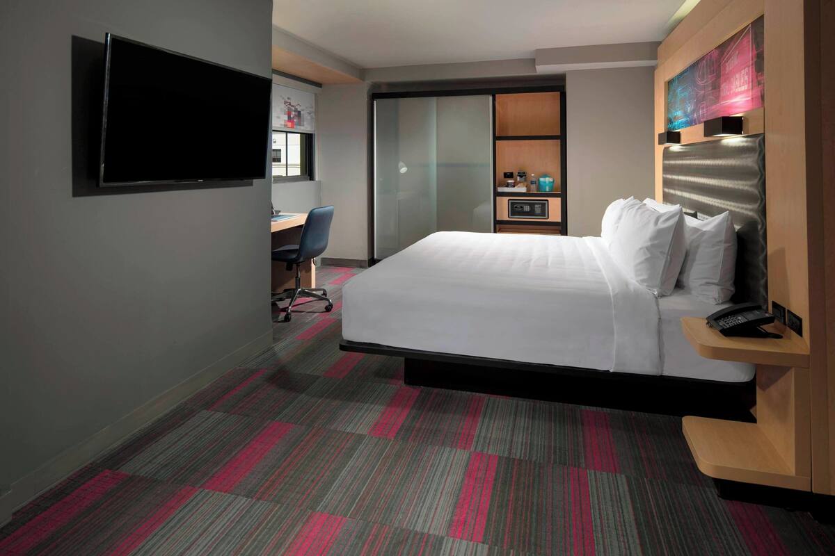 A hotel room with a bed, a desk, a chair, a TV, and a sliding door.