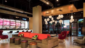 A modern lounge area with a red sofa, red chairs, and a bar with illuminated shelves. - Aloft by Marriott Coral Gables (Coral Gables)