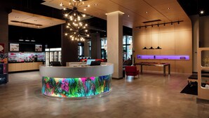 A modern hotel lobby with a reception desk, a pool table, and a lounge area with a purple-lit bar. - Aloft by Marriott Coral Gables (Coral Gables)