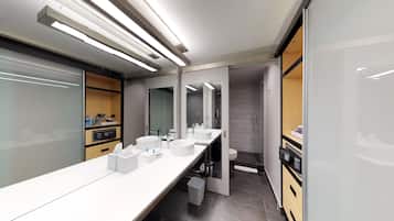 A modern bathroom with a long vanity, two sinks, a mirror, and a toilet.
