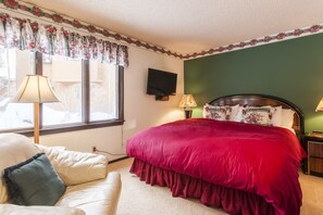 A bedroom with a large bed, a television mounted on the wall, and a window with curtains. - Chateau Sans Nom 17 (Mammoth Lakes)