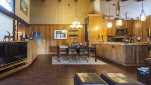 Uma cozinha ampla com armários de madeira, um espaço de refeições com mesa e cadeiras, e uma televisão de tela plana grande.