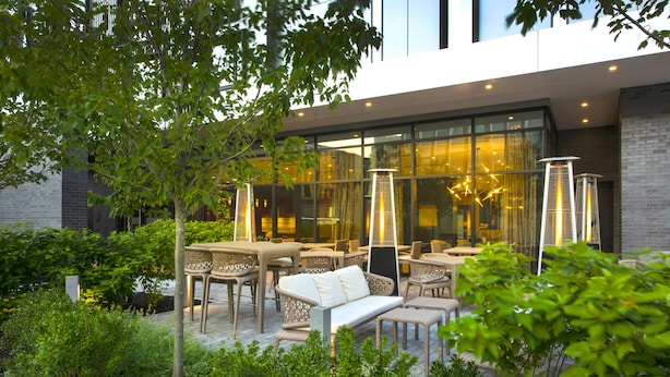 An outdoor seating area with wicker furniture and a glass building in the background. - AC Hotel by Marriott Boston Downtown (Boston)
