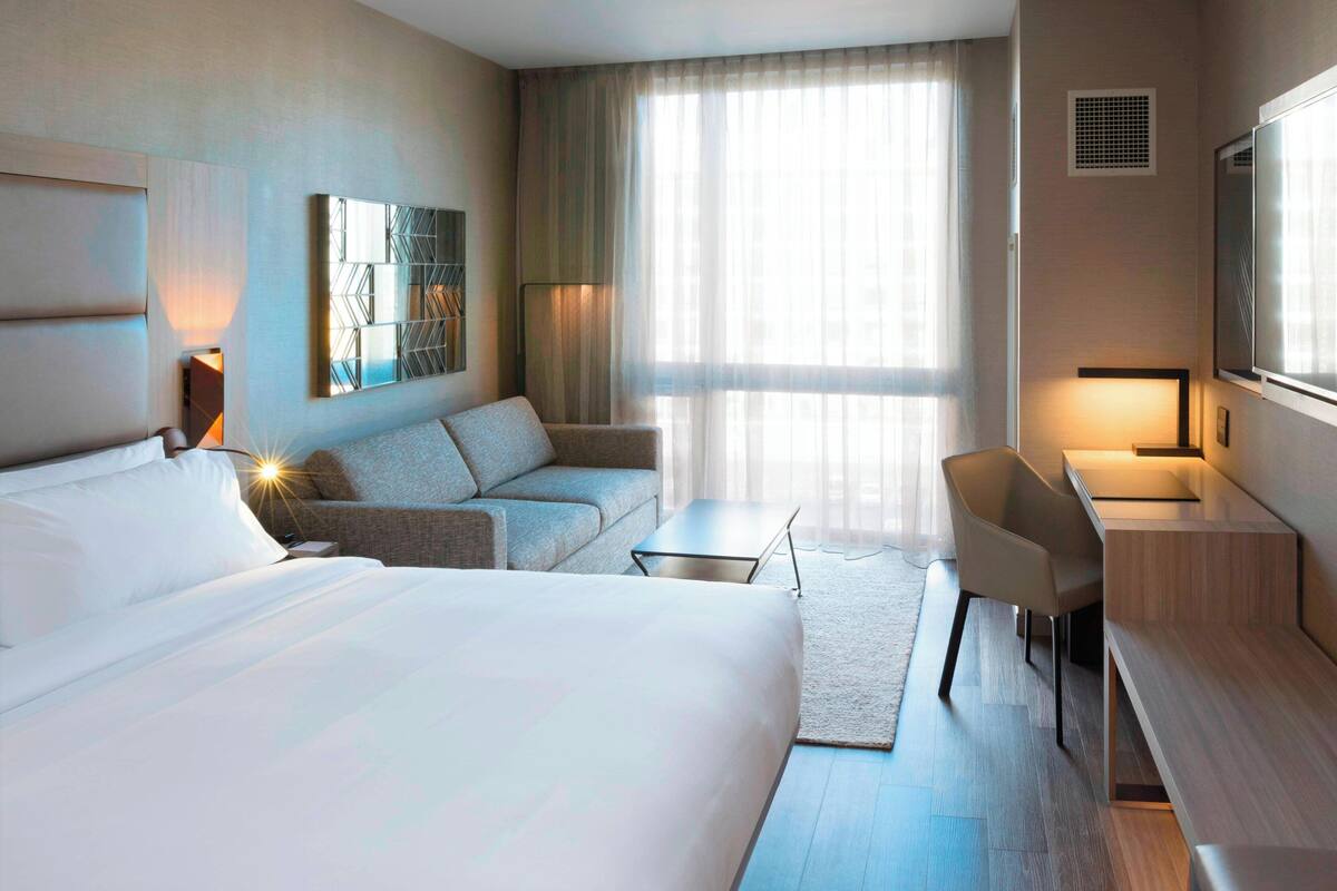 Hotellihuone, jossa on suuri sänky, sohva, työpöytä tuolilla ja televisio.