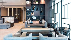 A modern living room with a sofa, armchairs, and a coffee table. There is a bookshelf with decorative items and a large window providing natural light. - AC Hotel by Marriott Boston Downtown (Boston)