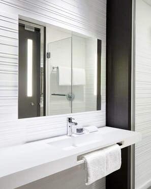 A modern bathroom with a large mirror, a white sink, and a towel hanging on the wall. - AC Hotel by Marriott Oklahoma City Bricktown (Oklahoma City)