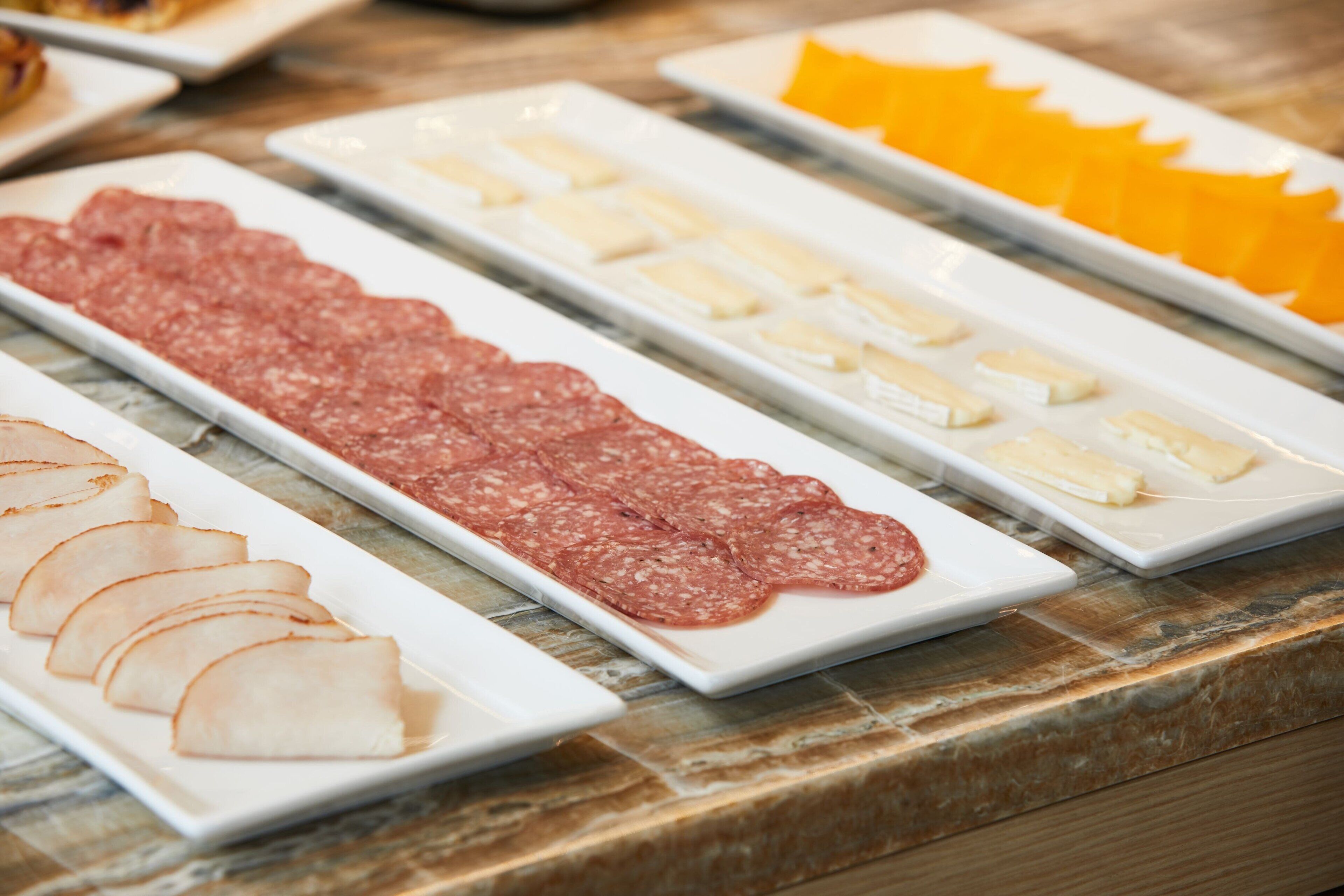 Una mesa de buffet con diversos alimentos, incluyendo carnes frías, quesos y frutas.