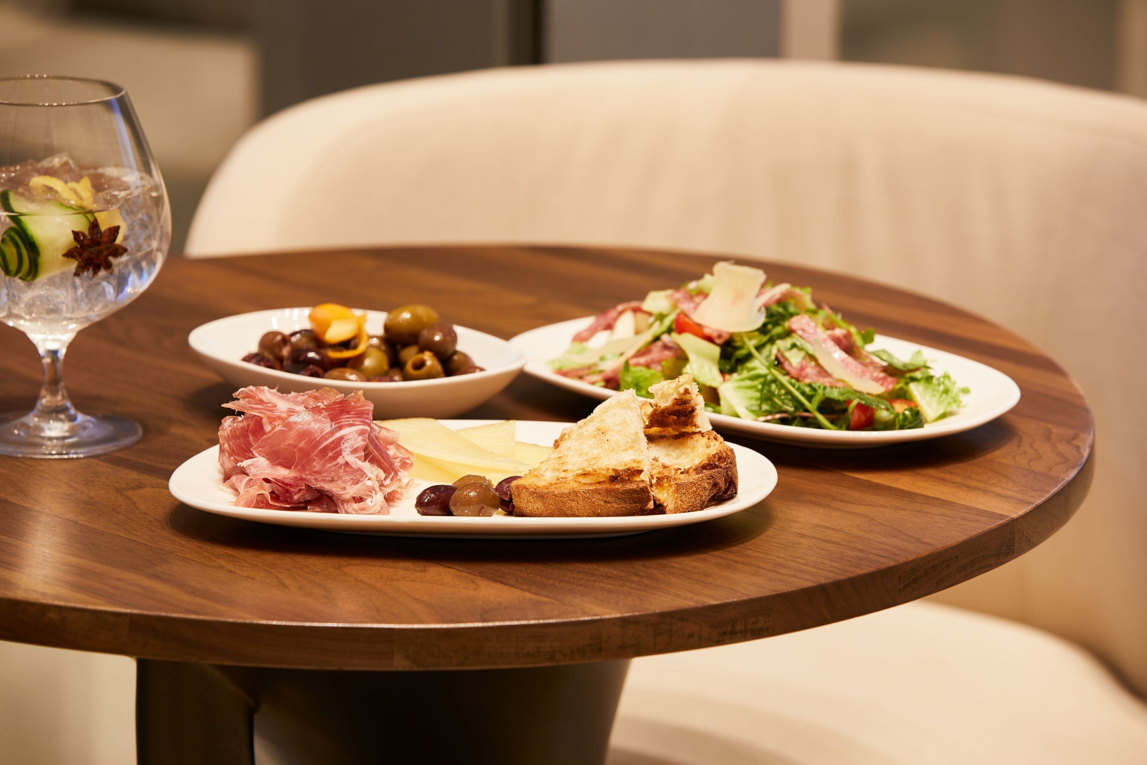 A dining table with plates of food, including olives, cheese, and a salad, and a glass of water.