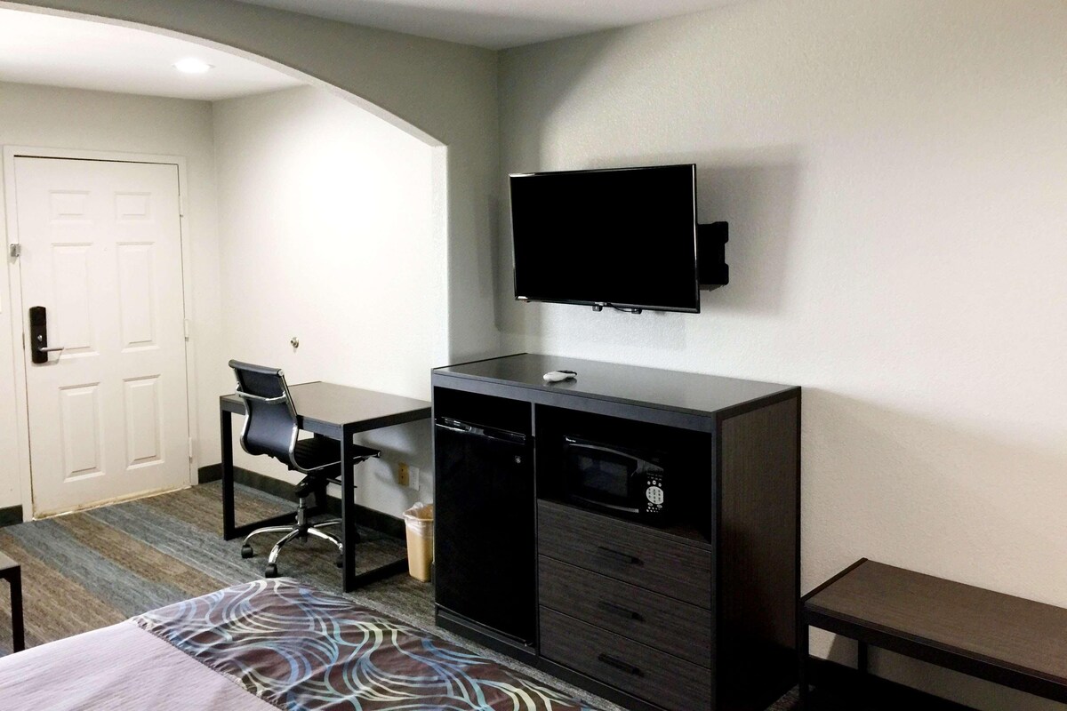 Una habitación de hotel con cama, escritorio, silla, televisor y microondas.
