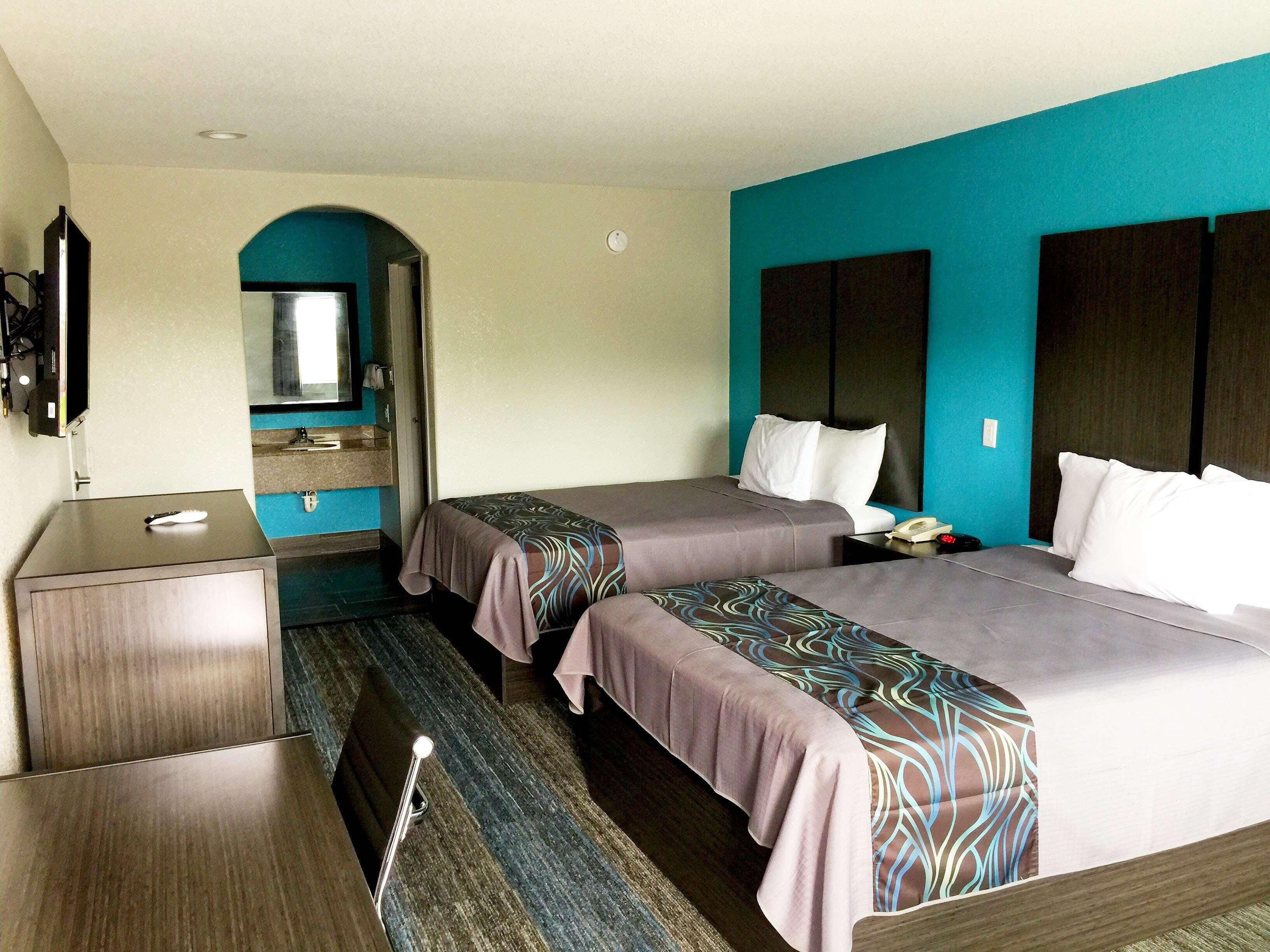 Habitación de hotel con dos camas, un escritorio, un espejo y un televisor.