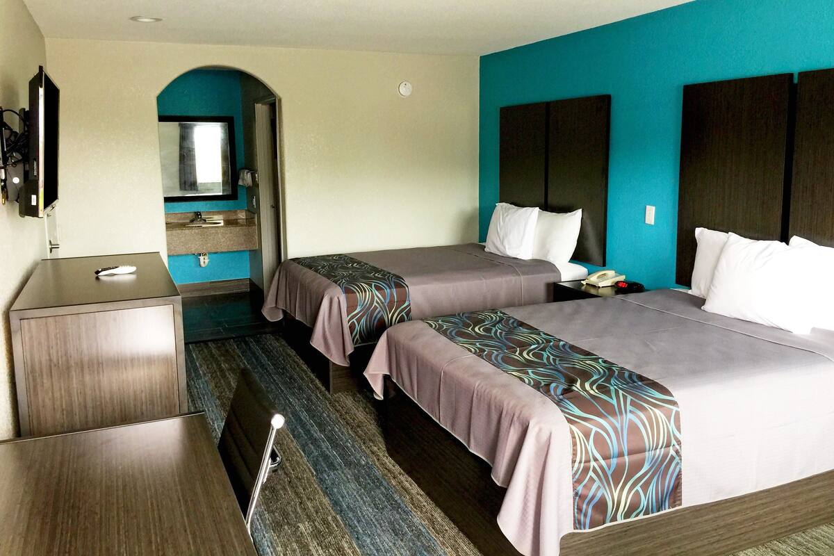 A hotel room with two beds, a desk, a mirror, and a TV.