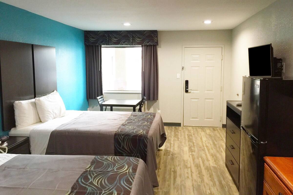 A hotel room with two beds, a desk, a chair, a television, and a wardrobe.
