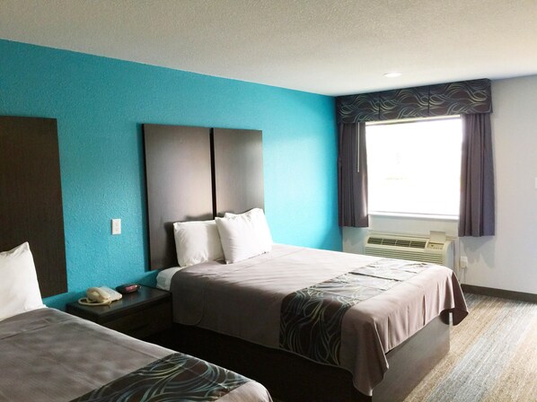 A hotel room with two beds, a large window with curtains, a wall-mounted air conditioner, and a telephone on the nightstand.