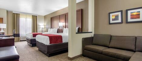 A hotel room with a large bed, a sofa, a desk, and two framed pictures on the wall.
