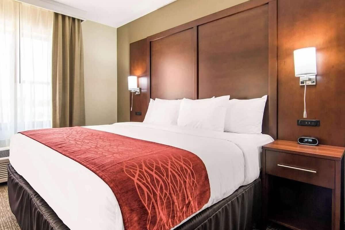 Habitación de hotel con una cama grande, una mesita de noche con un reloj y una lámpara fijada a la pared.