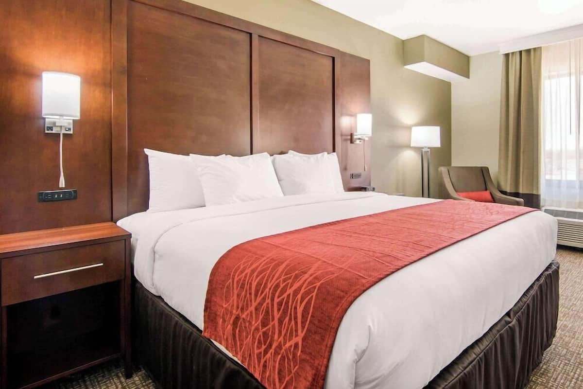 Una habitación de hotel con una cama grande, una mesita de noche, una silla y dos lámparas fijadas a la pared.