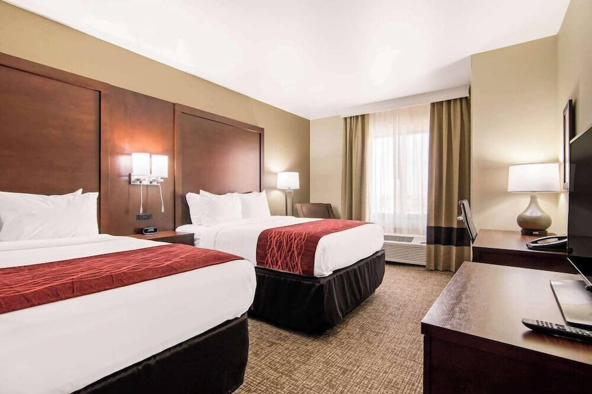 Habitación de hotel con dos camas, un escritorio, un televisor y una ventana con cortinas.