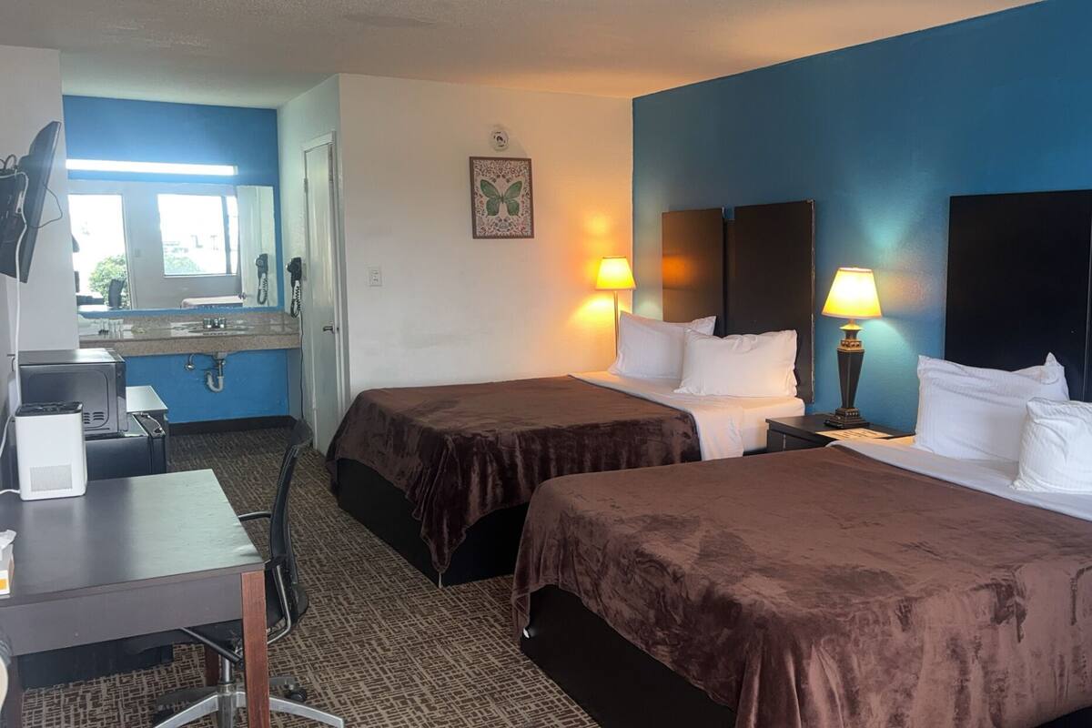 A hotel room with two beds, a desk, a chair, a mirror, and a window.