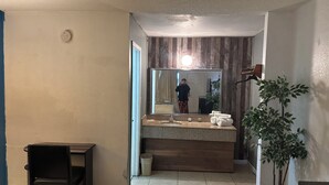 A bathroom with a wooden vanity, a mirror, a sink, and a potted plant. - Americas Best Value Inn Brinkley (Brinkley)