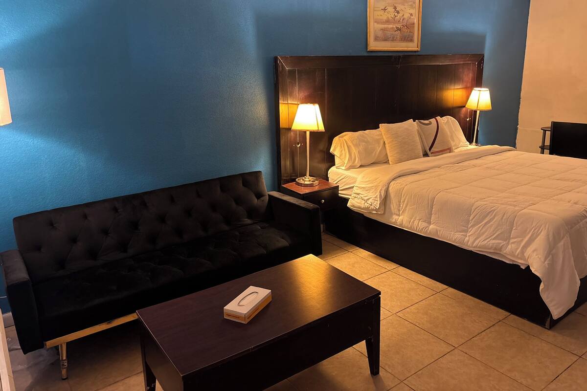 A hotel room with a large bed, two bedside lamps, a dark sofa, and a small table with a book.