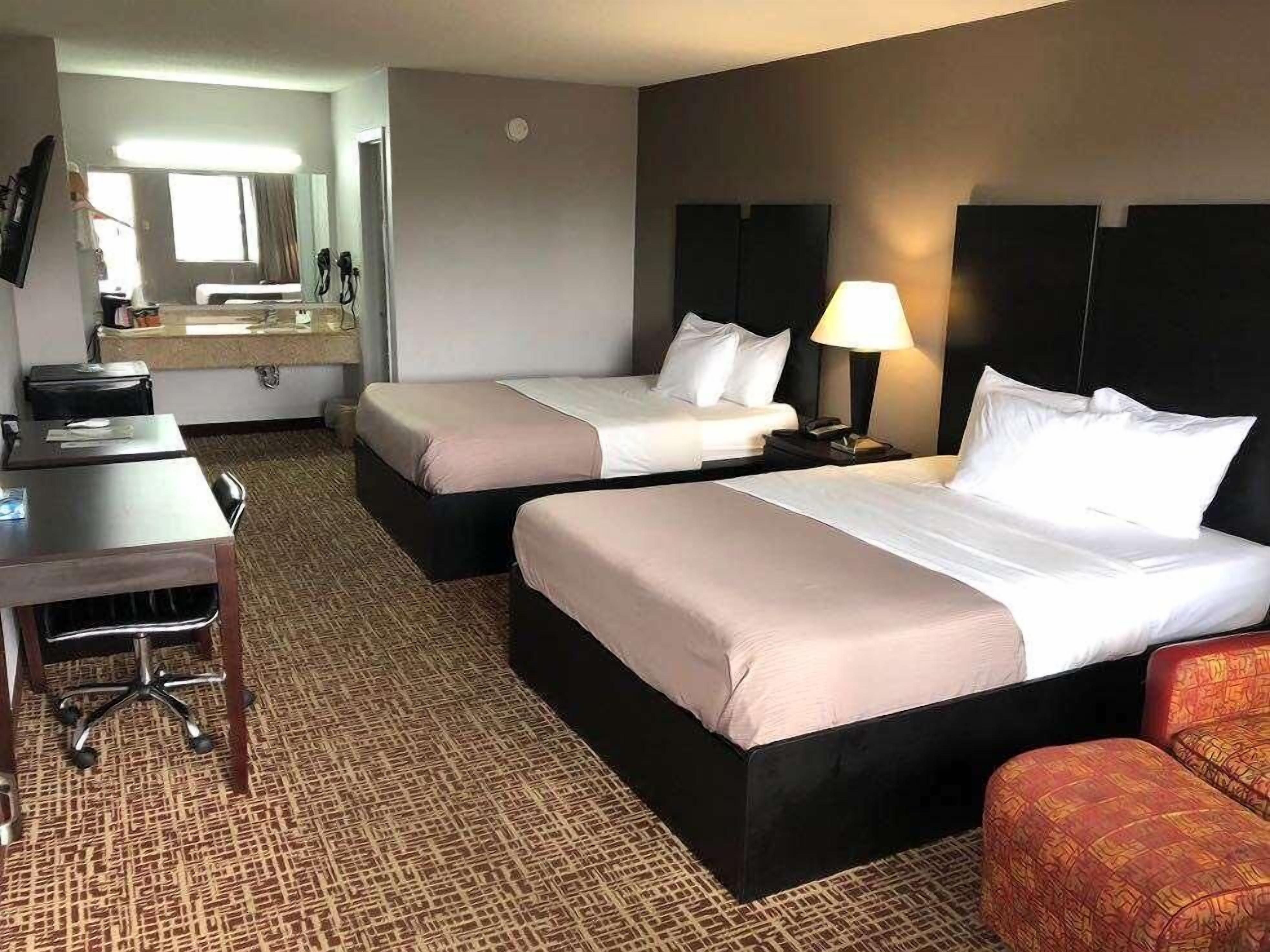 Ein Hotelzimmer mit zwei Betten, einem Schreibtisch, einem Stuhl, einer Lampe und einem Spiegel.