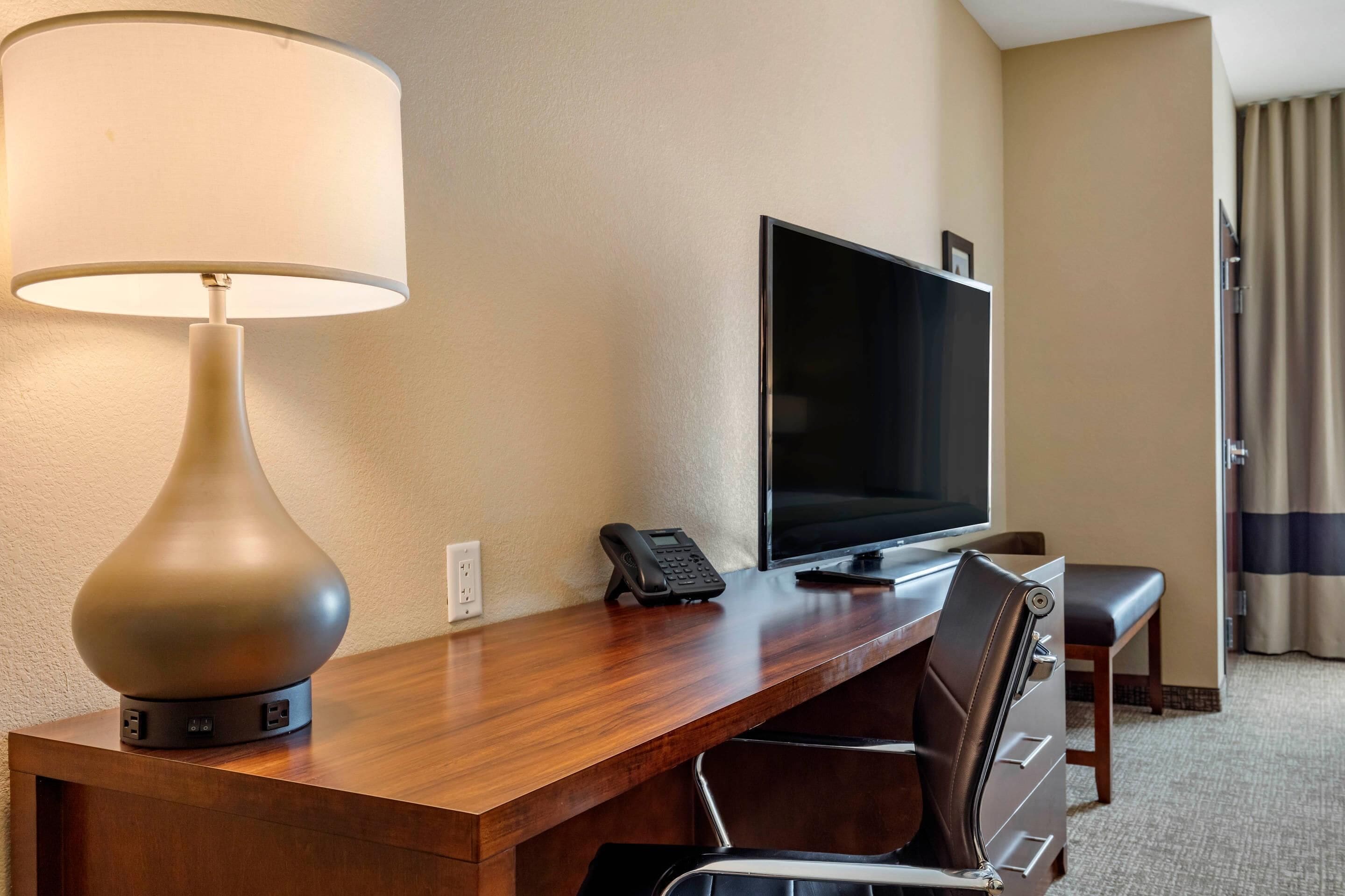 A hotel room with a wooden desk, a television, a telephone, and a chair.