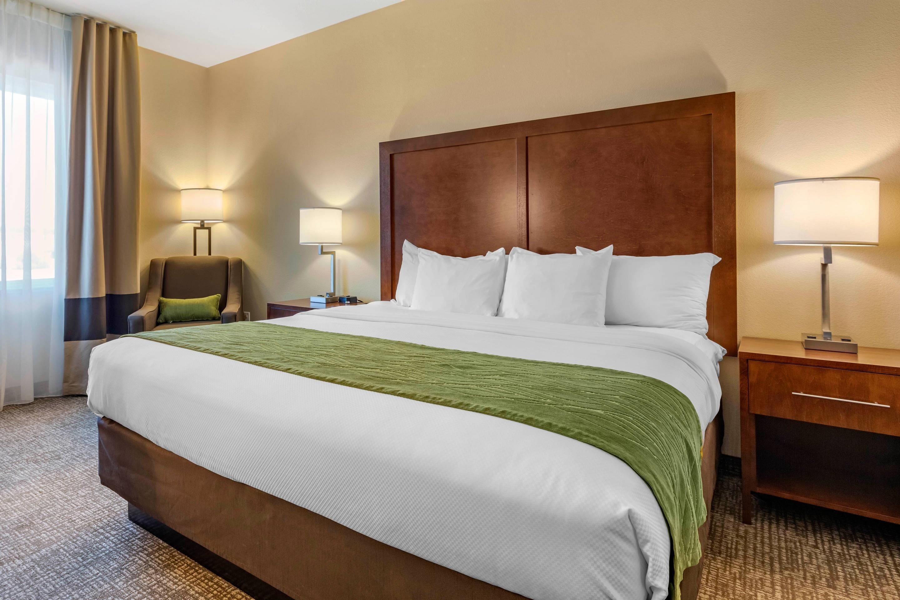 Habitación de hotel con una cama grande, dos lámparas de noche, una silla y una mesita de noche.