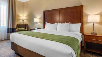 Habitación de hotel con una cama grande, dos lámparas de noche, una silla y una mesita de noche.