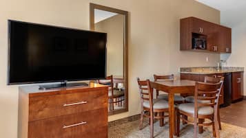 Habitación de hotel con televisión de pantalla plana, muebles de madera, zona de cocina y un espejo grande.